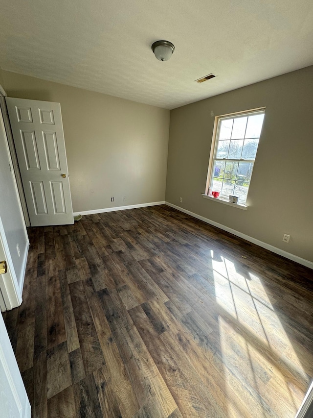 unfurnished room featuring visible vents, baseboards, and dark wood-style floors