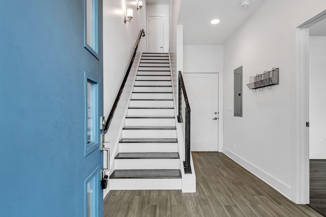 staircase with recessed lighting, electric panel, wood finished floors, and baseboards