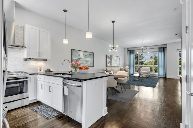 kitchen with a sink, dark countertops, appliances with stainless steel finishes, a peninsula, and wall chimney range hood