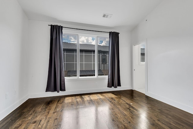 spare room with wood finished floors, visible vents, and baseboards