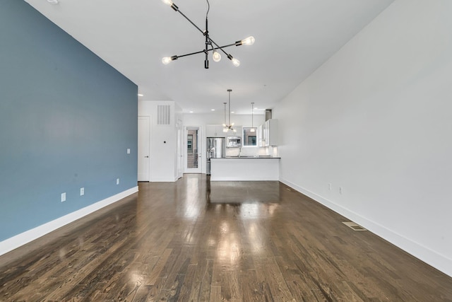 unfurnished living room with dark wood-style floors, visible vents, baseboards, and an inviting chandelier