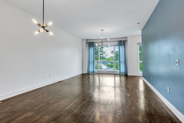 unfurnished room featuring dark wood finished floors, an inviting chandelier, and baseboards