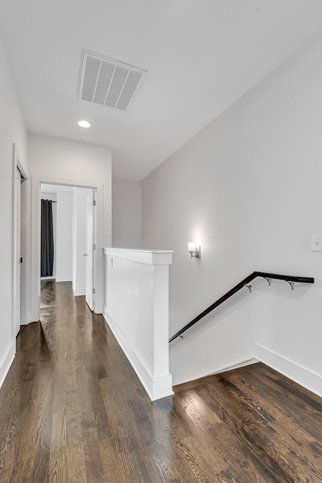 hallway with visible vents, an upstairs landing, baseboards, and wood finished floors