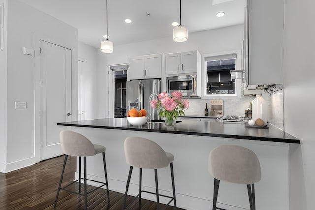 kitchen featuring tasteful backsplash, dark countertops, appliances with stainless steel finishes, a peninsula, and dark wood-style flooring