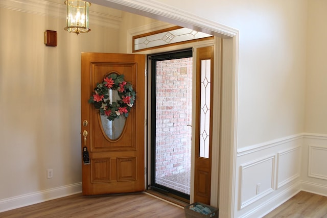 foyer entrance featuring light wood finished floors, a decorative wall, wainscoting, and a chandelier