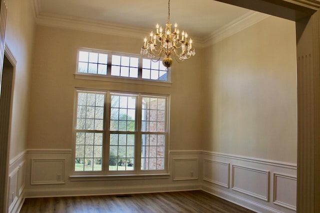 empty room featuring dark wood finished floors, a notable chandelier, wainscoting, and ornamental molding