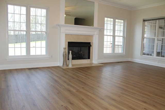 unfurnished living room with wood finished floors, visible vents, baseboards, a high end fireplace, and crown molding