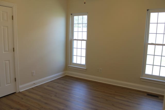 unfurnished room featuring dark wood-type flooring, visible vents, and baseboards