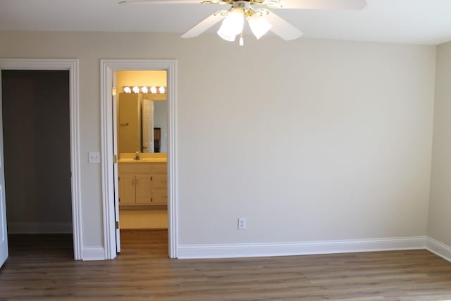 unfurnished bedroom featuring a sink, ensuite bathroom, baseboards, and wood finished floors