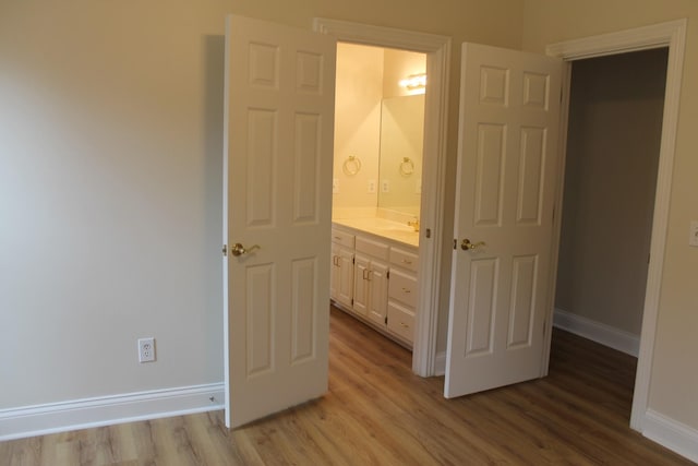 unfurnished bedroom featuring a sink, connected bathroom, baseboards, and light wood finished floors