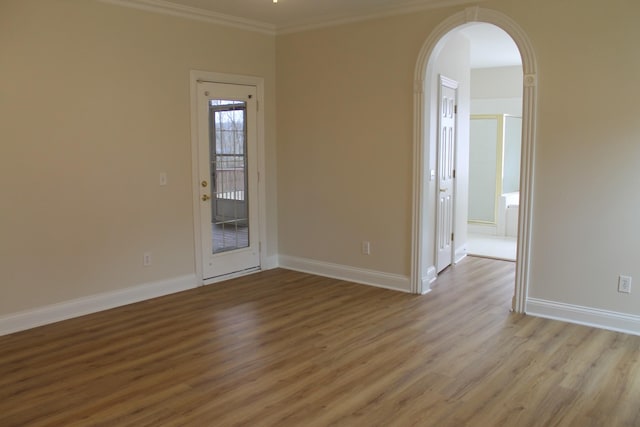 unfurnished room featuring arched walkways, light wood finished floors, crown molding, and baseboards