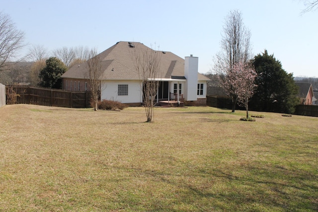 rear view of property with a yard, a chimney, and fence