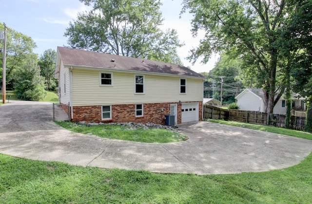 view of side of home featuring central AC unit, fence, driveway, a garage, and a lawn