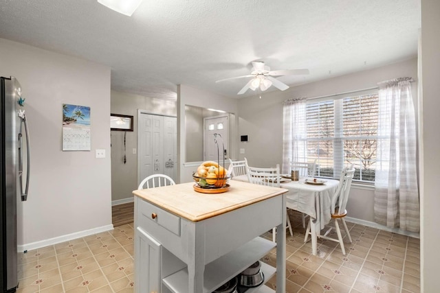 kitchen featuring baseboards, a textured ceiling, ceiling fan, and freestanding refrigerator