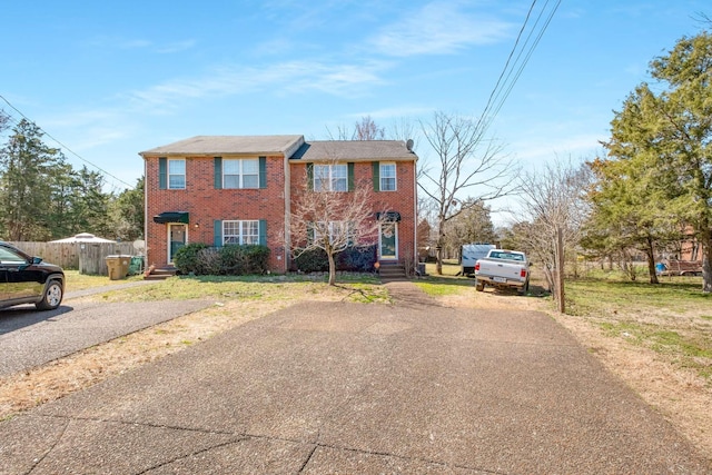 colonial house with brick siding, driveway, and fence