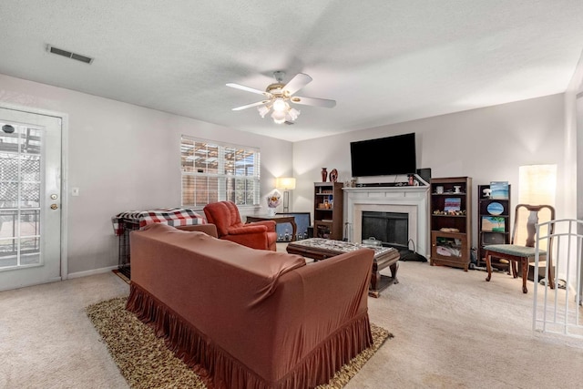 living area with light carpet, visible vents, a fireplace, and ceiling fan