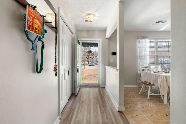 hall with visible vents, a textured ceiling, light wood-style floors, and baseboards