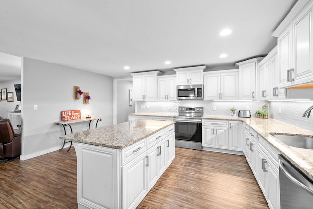 kitchen with a sink, stainless steel appliances, wood finished floors, and white cabinets