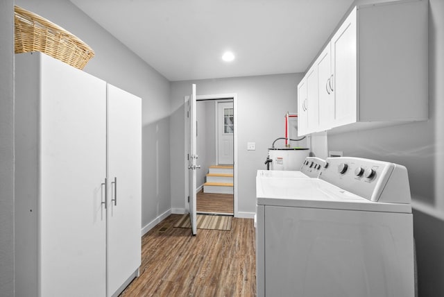 washroom with wood finished floors, washing machine and dryer, water heater, cabinet space, and baseboards