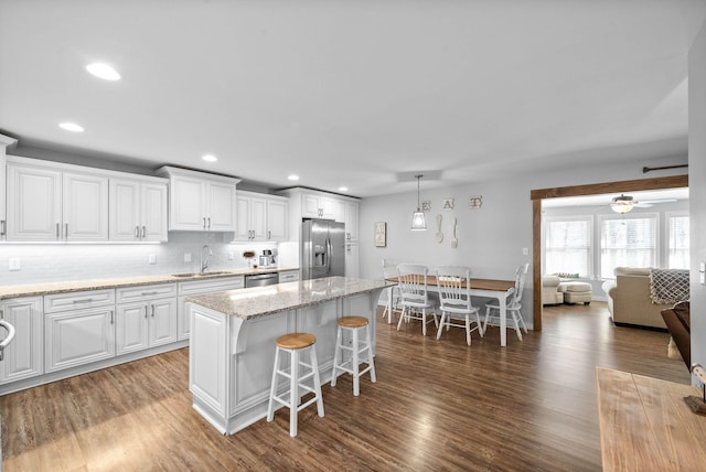 kitchen with wood finished floors, white cabinetry, a kitchen island, stainless steel appliances, and a kitchen bar