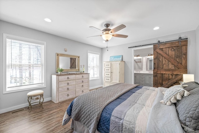 bedroom with visible vents, baseboards, a barn door, recessed lighting, and wood finished floors