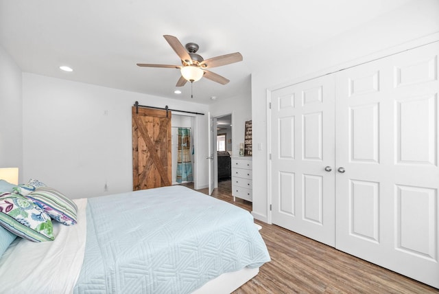 bedroom with ceiling fan, a barn door, recessed lighting, wood finished floors, and a closet