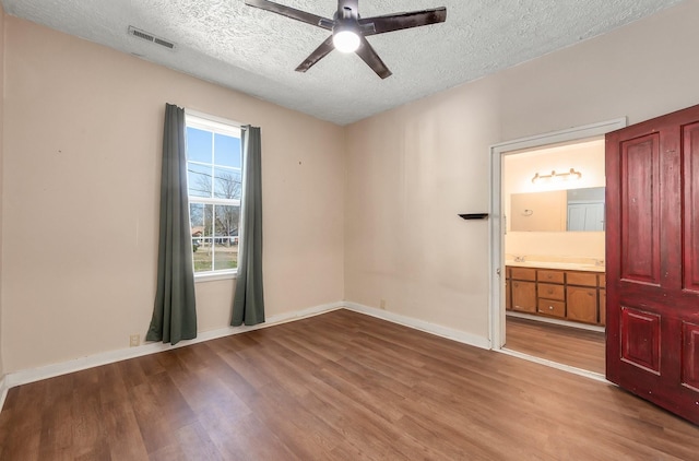 unfurnished room featuring visible vents, a ceiling fan, a textured ceiling, wood finished floors, and baseboards