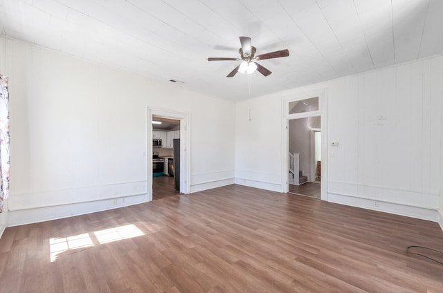 empty room featuring a ceiling fan, stairs, wood finished floors, and visible vents