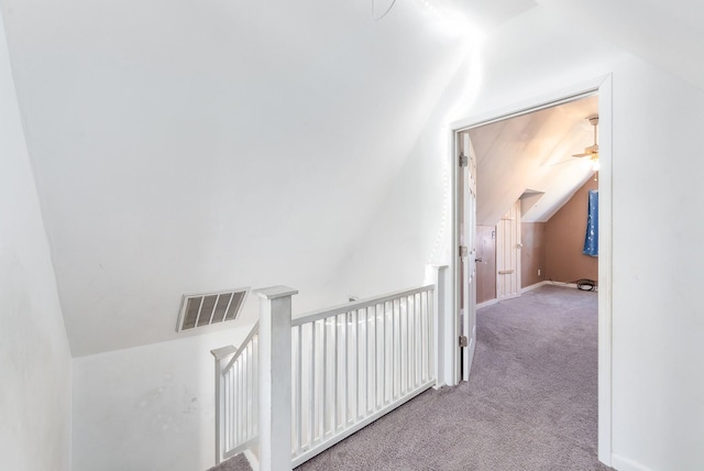 hall featuring lofted ceiling, an upstairs landing, visible vents, and carpet floors