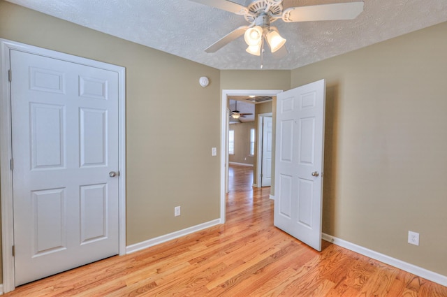 unfurnished bedroom featuring a textured ceiling, light wood-type flooring, baseboards, and a ceiling fan