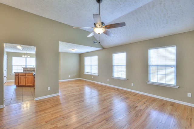 unfurnished room with light wood finished floors, visible vents, a healthy amount of sunlight, ceiling fan with notable chandelier, and a textured ceiling