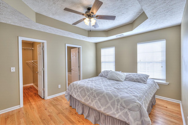 bedroom with a walk in closet, a raised ceiling, light wood finished floors, and a textured ceiling