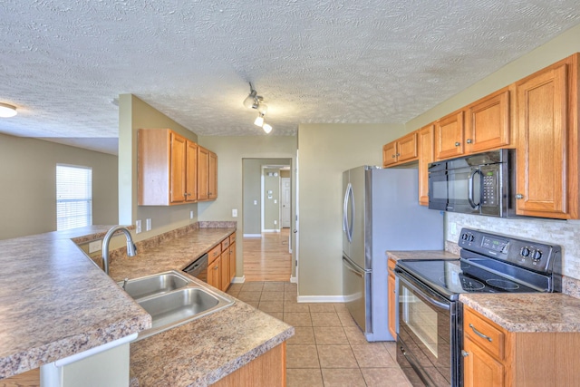 kitchen with light tile patterned floors, a peninsula, a sink, black appliances, and light countertops