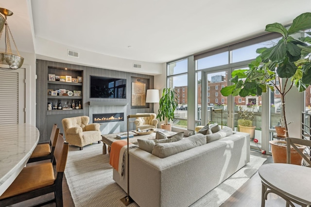 living area featuring visible vents, built in features, a glass covered fireplace, and expansive windows