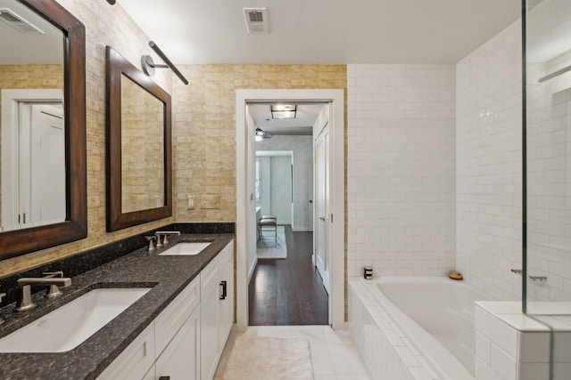 bathroom with visible vents, tiled tub, and a sink