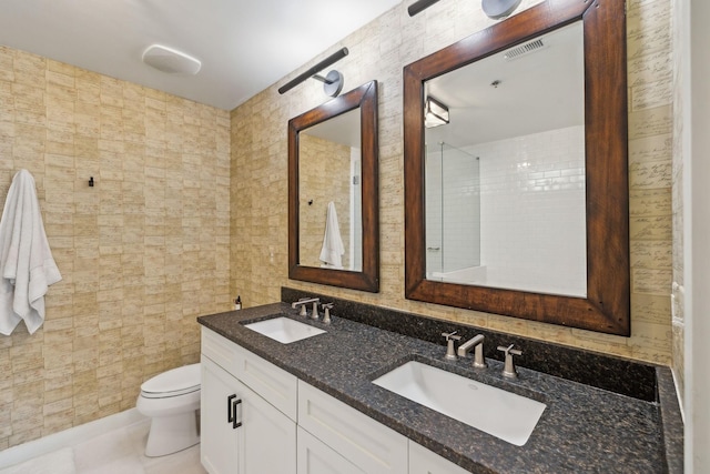 bathroom with tile walls, toilet, double vanity, and a sink