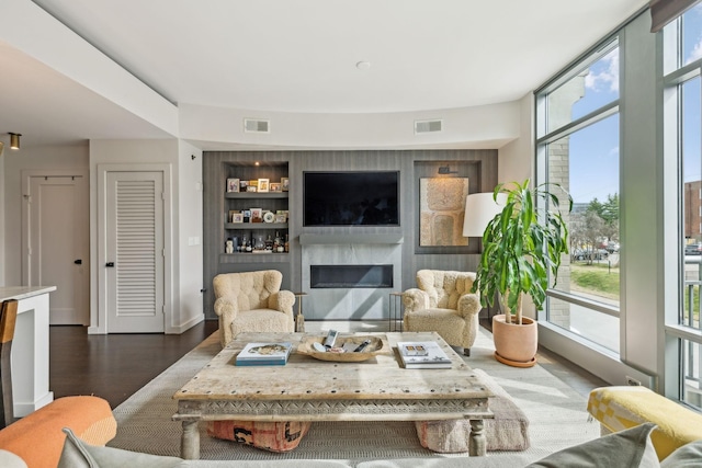 living room featuring a glass covered fireplace, a wall of windows, visible vents, and dark wood-style flooring