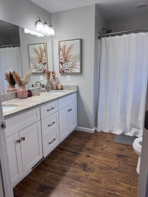 full bath featuring toilet, a shower with shower curtain, double vanity, wood finished floors, and a sink