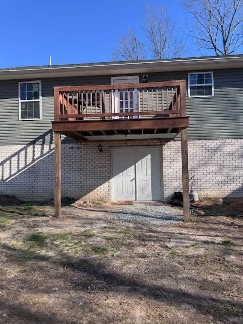 rear view of house featuring brick siding, an attached garage, driveway, and a deck