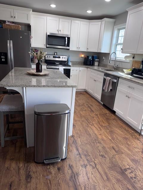 kitchen with a sink, a kitchen island, dark wood-style floors, stainless steel appliances, and white cabinets