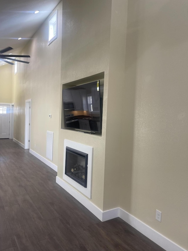 unfurnished living room featuring visible vents, baseboards, a towering ceiling, and dark wood-style flooring