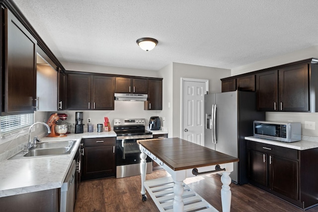 kitchen featuring dark wood-type flooring, under cabinet range hood, dark brown cabinetry, appliances with stainless steel finishes, and a sink