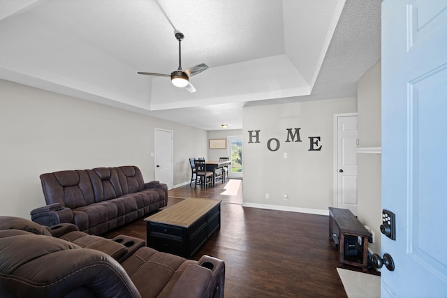 living room featuring baseboards, a tray ceiling, a textured ceiling, a ceiling fan, and dark wood-style flooring