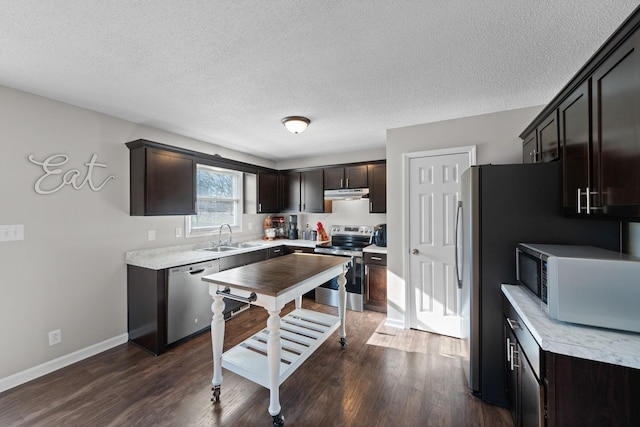 kitchen featuring dark wood-type flooring, under cabinet range hood, dark brown cabinetry, stainless steel appliances, and a sink