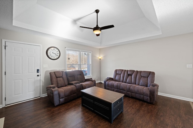 living area with a raised ceiling, baseboards, dark wood-style flooring, and ceiling fan