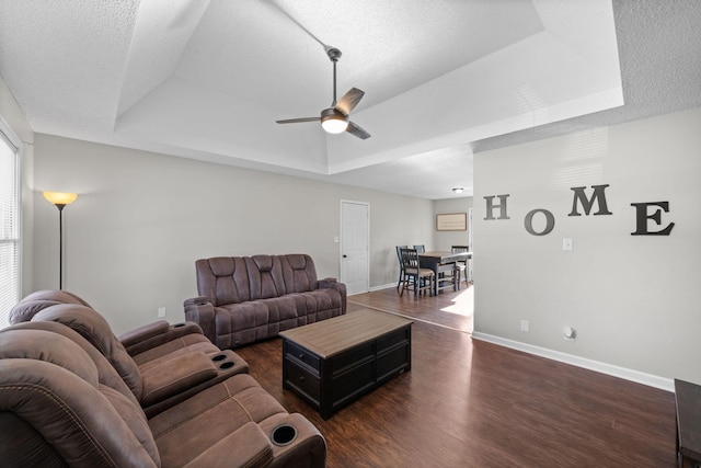 living area with baseboards, a textured ceiling, a tray ceiling, and dark wood-style flooring