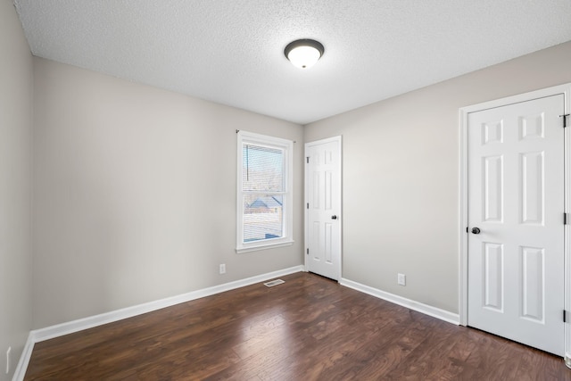 unfurnished bedroom with visible vents, dark wood-style floors, baseboards, and a textured ceiling