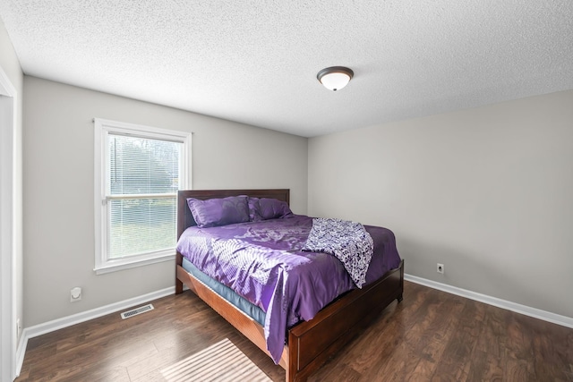 bedroom with visible vents, a textured ceiling, baseboards, and wood finished floors