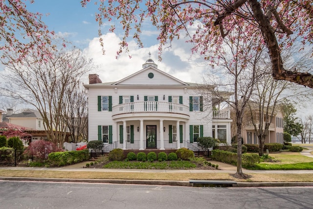 greek revival inspired property with a balcony, covered porch, a chimney, and fence