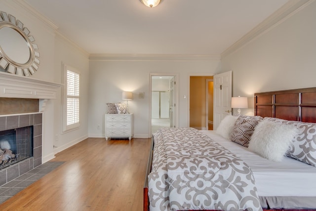 bedroom with ornamental molding, wood finished floors, baseboards, and a tile fireplace